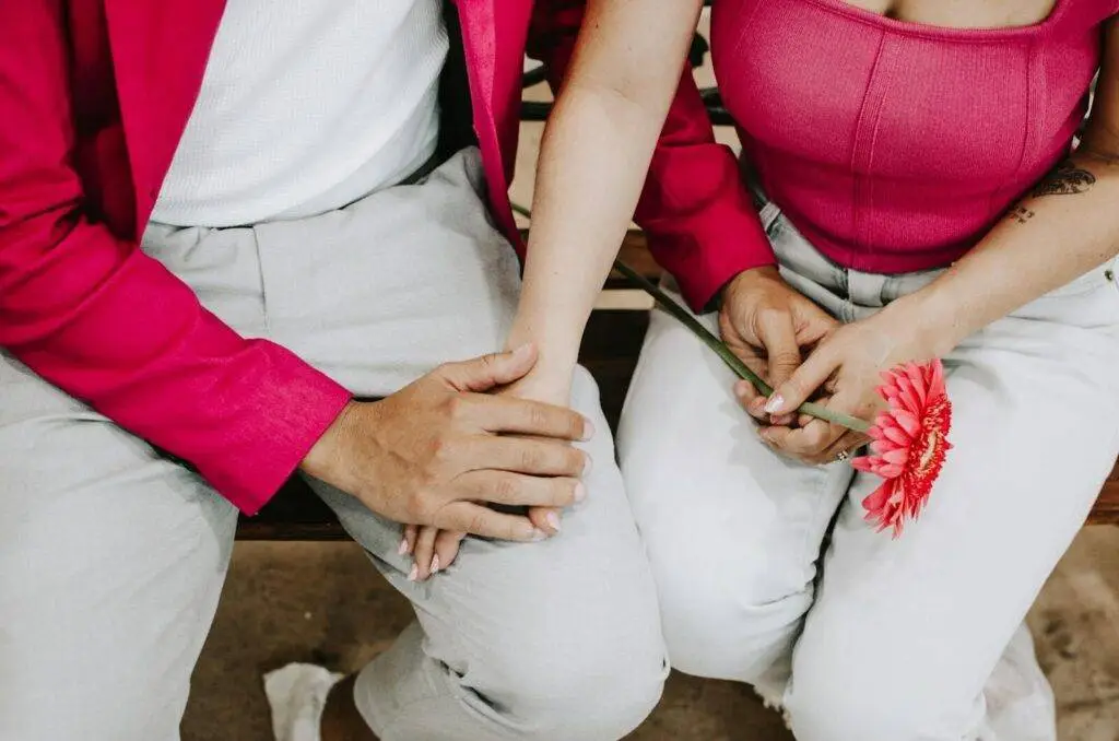 Close-up of a couple in pink attire holding hands and a pink flower, symbolizing romance.