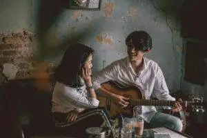 A couple enjoys an intimate music session indoors with a guitar.