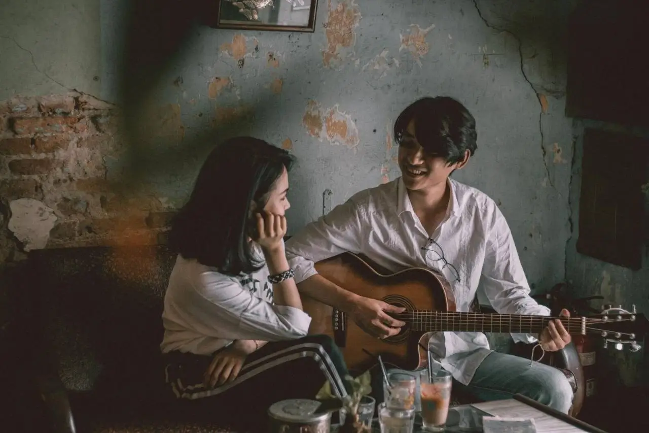 A couple enjoys an intimate music session indoors with a guitar.