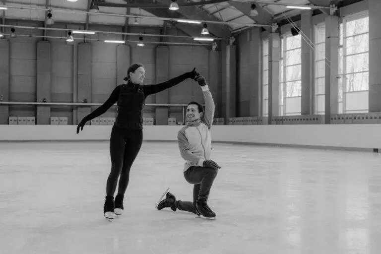 A couple showcases their ice skating skills in an indoor rink.