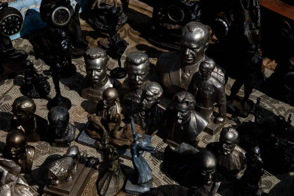 Diverse array of bronze sculptures and busts displayed outdoors, casting intricate shadows.
