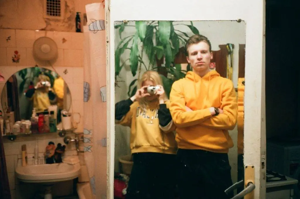 A couple in yellow hoodies takes a casual selfie in a bathroom mirror, embracing togetherness and everyday life.