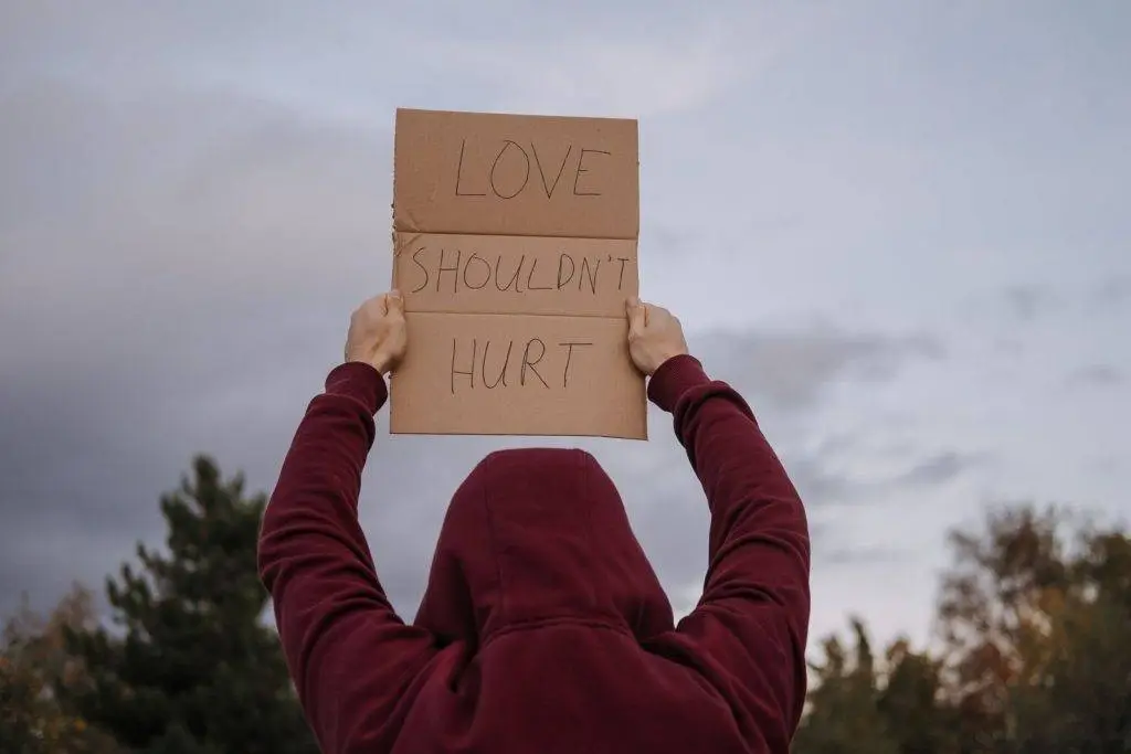 Back view of unrecognizable person in hoodie demonstrating carton placard with Love Should not Hurt inscription during anti violence protests
