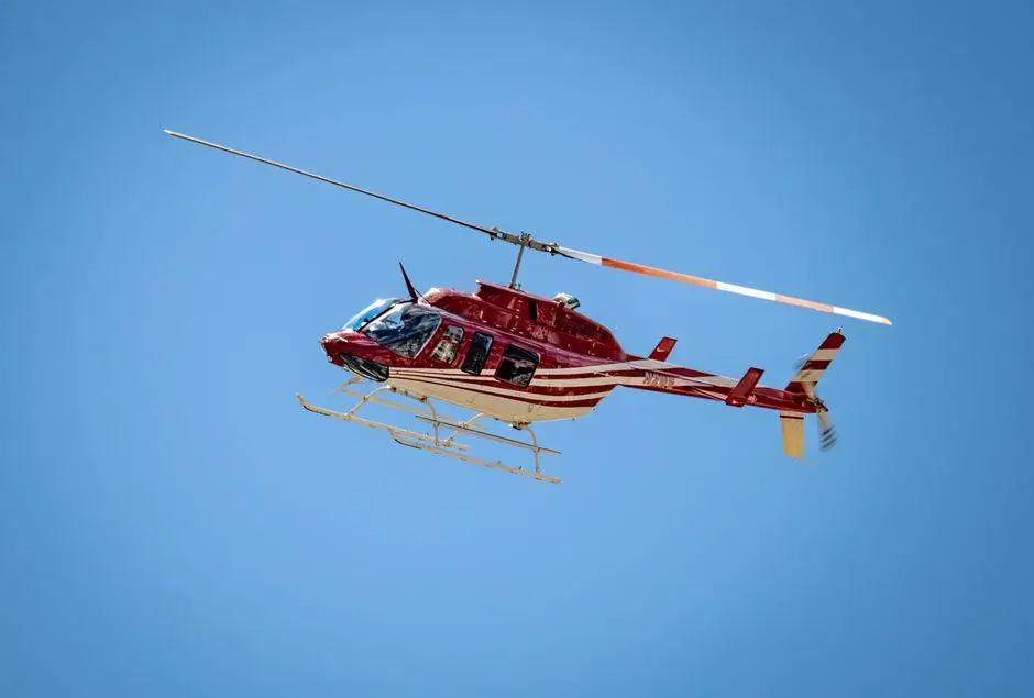 A red Bell 206 helicopter soaring against a clear blue sky, showcasing aviation in action.